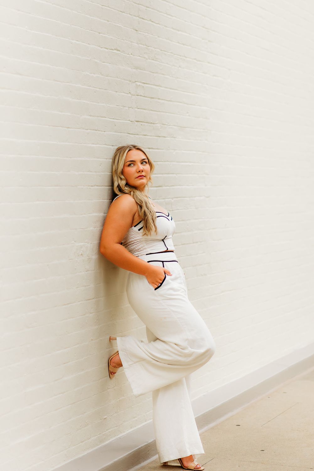 Fashion pose against white brick wall in white outfit with black trim.