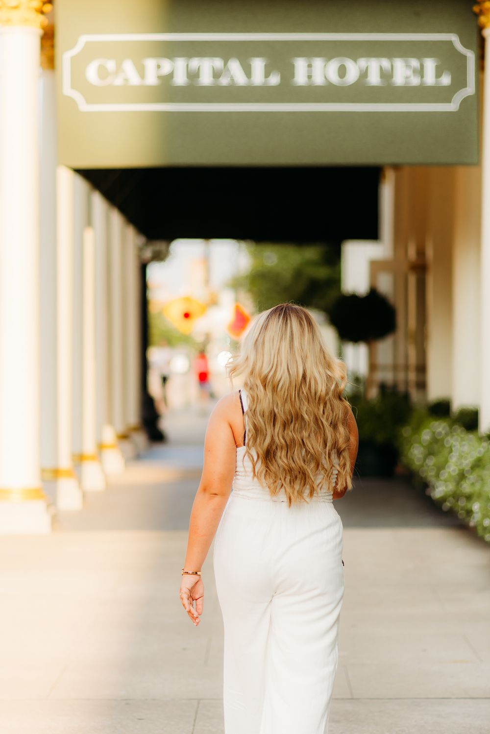 Back view of person in white dress walking under Capital Hotel sign.