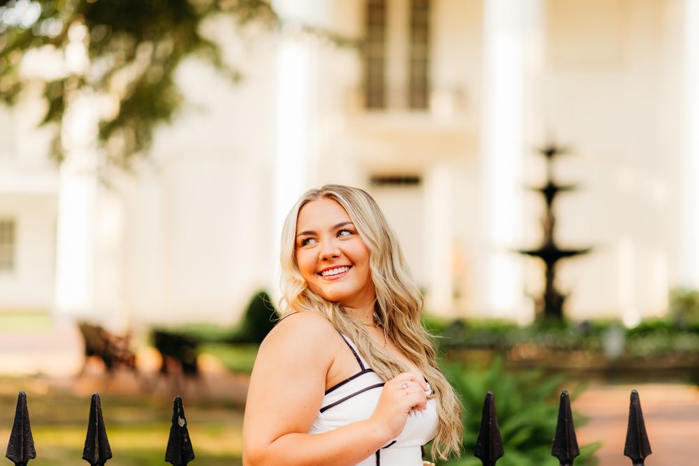 Portrait in front of decorative black iron fence and classic fountain at elegant venue.