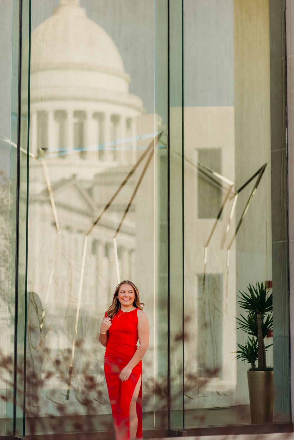 Woman in red dress posing by modern glass building with dome reflection.