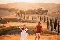 Two people admiring the scenic Tuscan countryside with rolling hills and cypress trees at sunset in Italy.