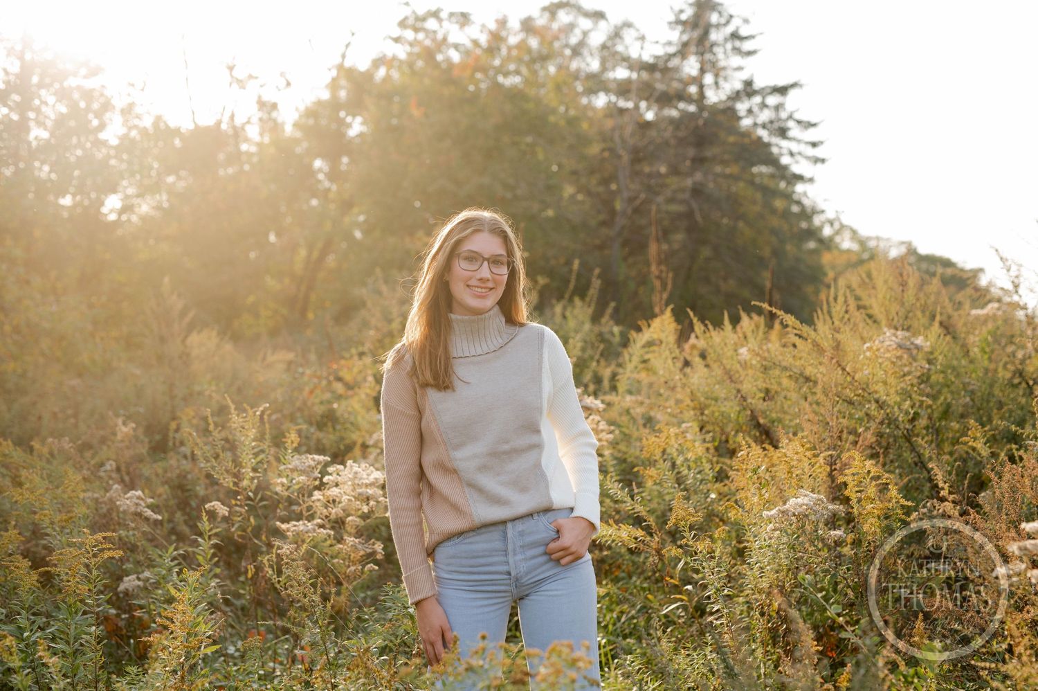 A person poses in casual attire among wild autumn foliage during golden hour.