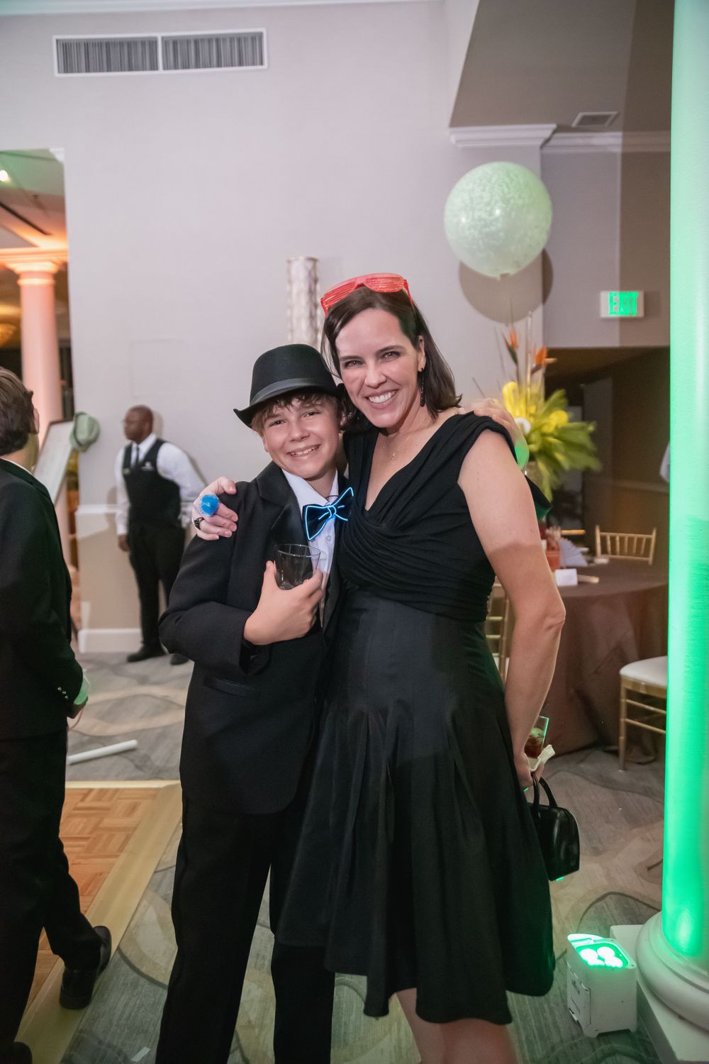 Two people in formal black attire pose at an elegant party with colored lighting.