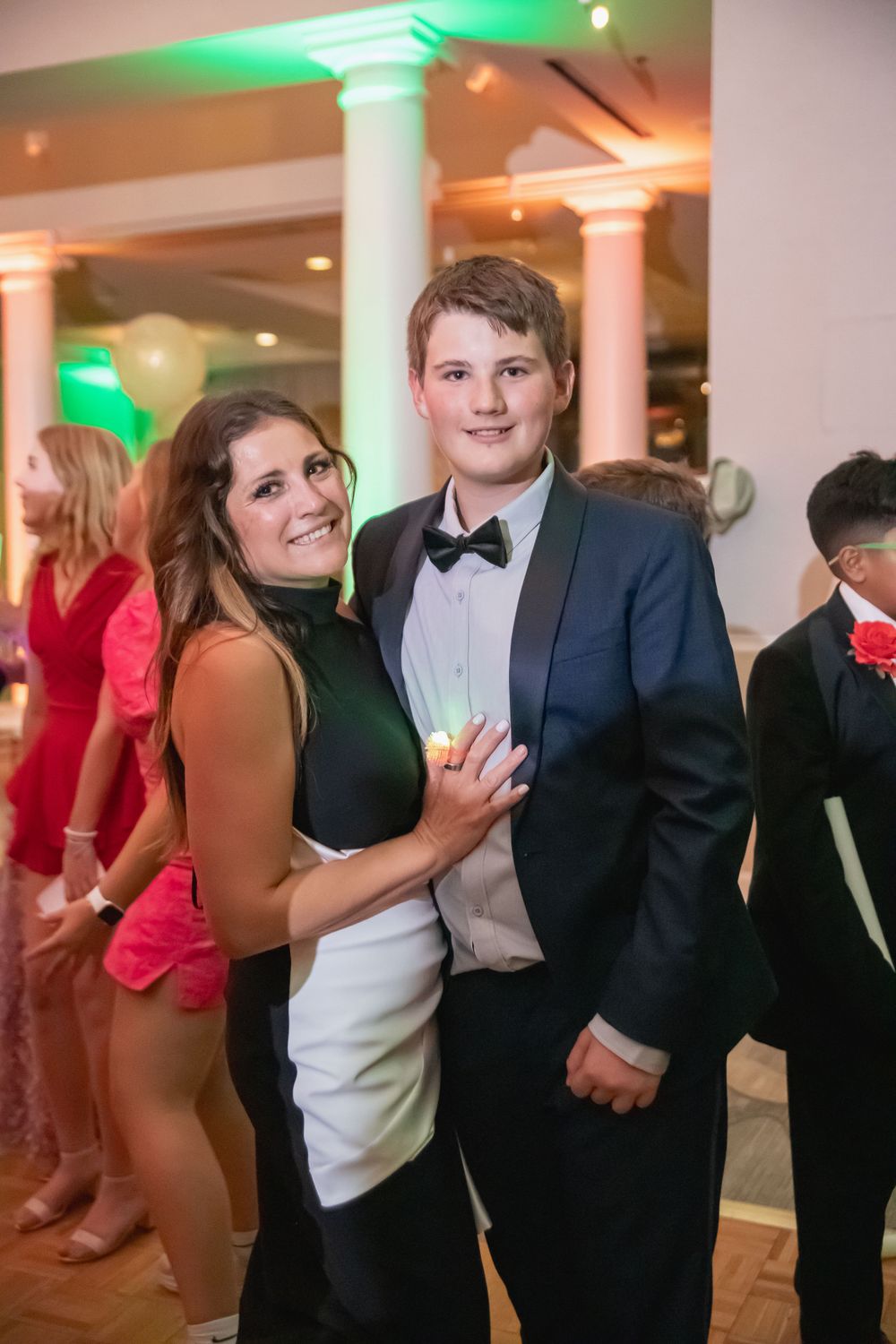 Couple in formal wear poses together at elegant event with decorative lighting.