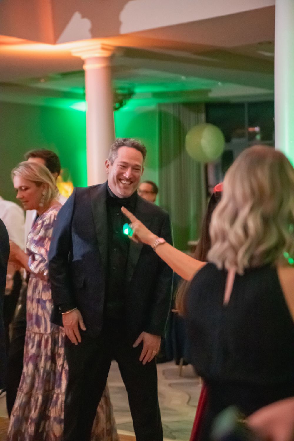 People dancing and enjoying themselves at a party with green and orange lighting.