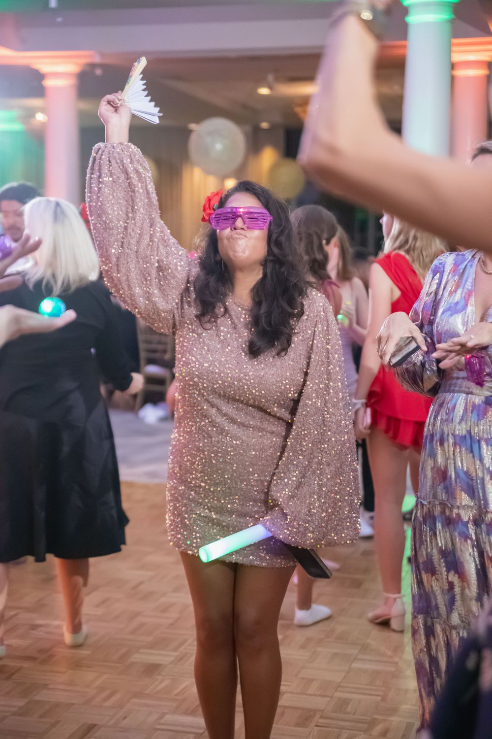 Person in sparkly dress dancing at party with colorful lighting and balloons.