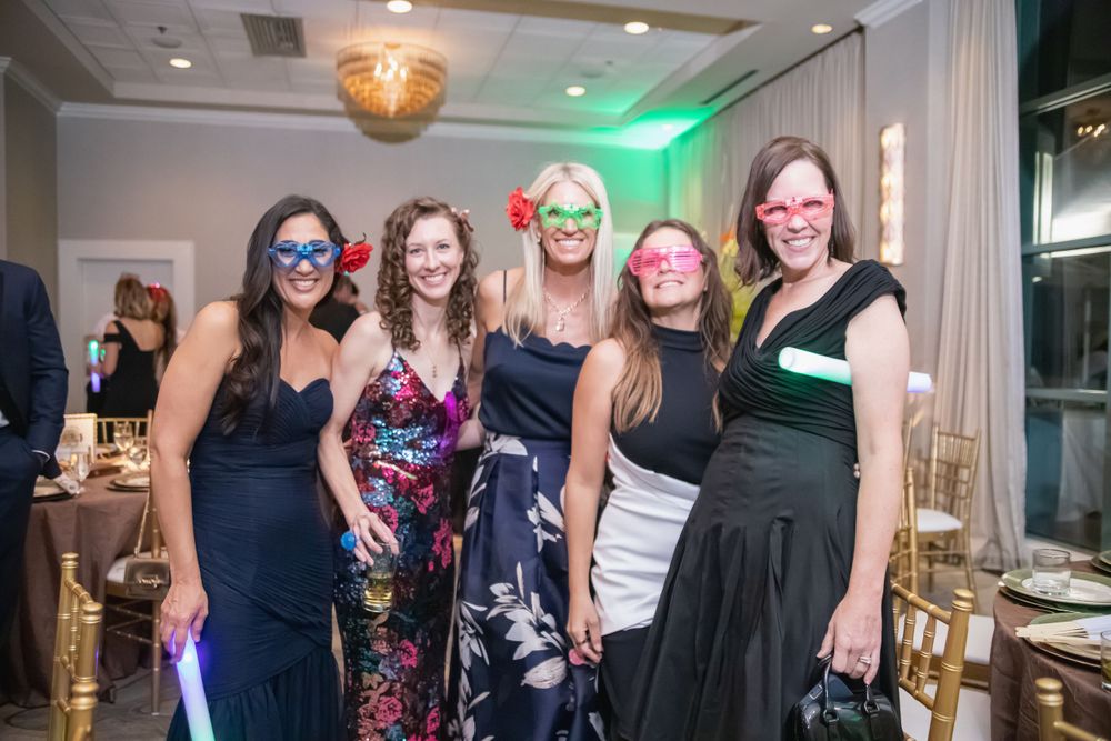 Group wearing formal attire and fun glasses poses at festive event with green lighting.