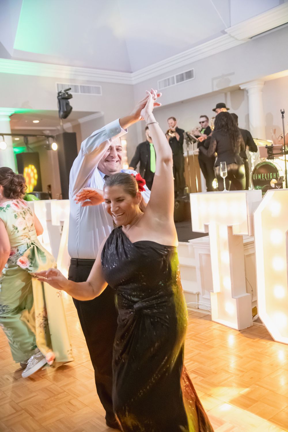 Energetic dancers move across a wooden dance floor with illuminated decor in the background.