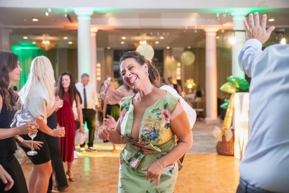 Wedding reception dance floor filled with joyful guests celebrating under green and pink lighting.