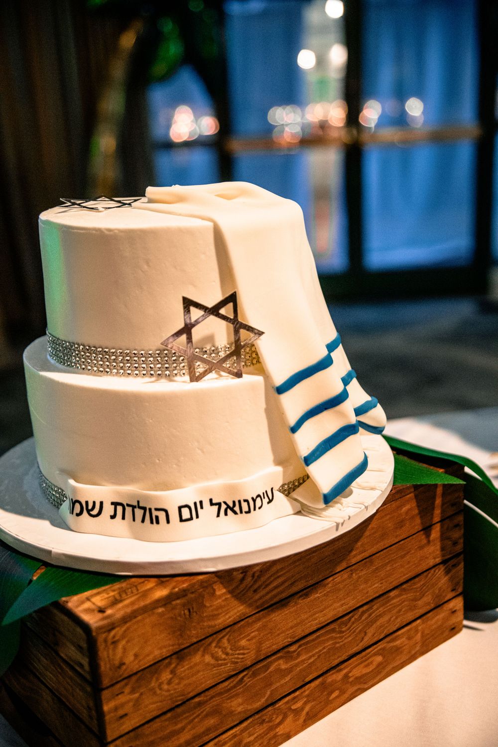 White tiered cake with blue stripes and bow details displayed on wooden stand.