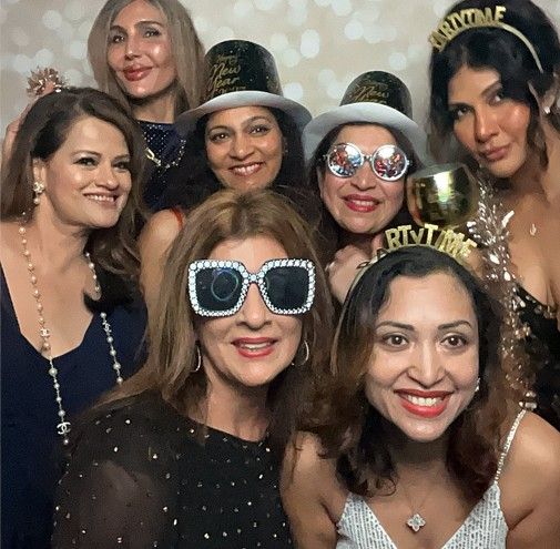 A group of women wearing party hats and sunglasses pose together for a celebratory photo.