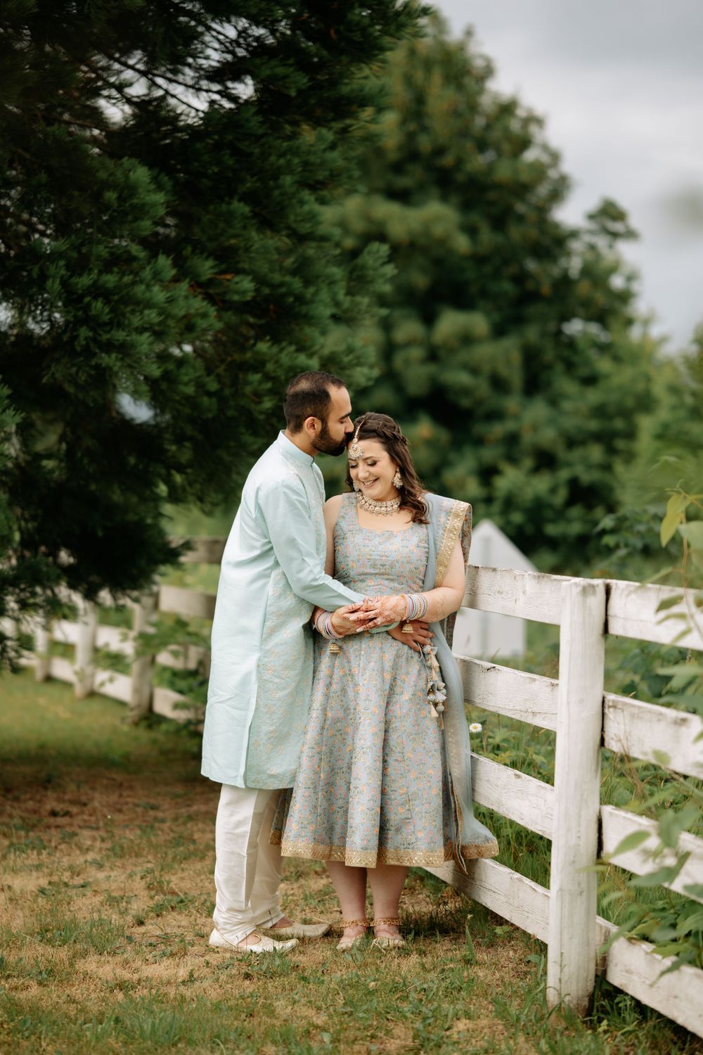 Romantic couple moment by white fence in countryside setting.