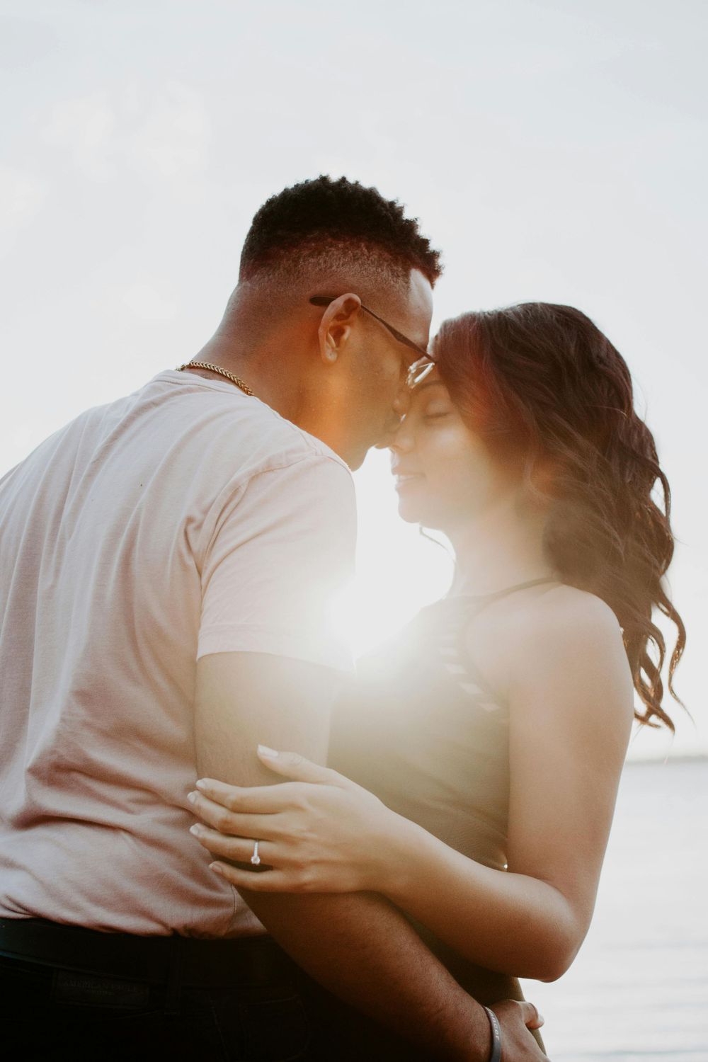 Backlit couple embracing in soft sunlight creating romantic silhouette against bright background.