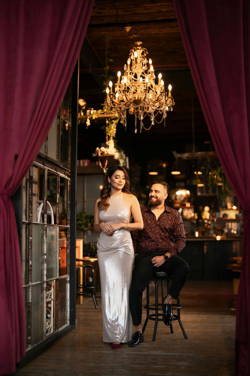 Elegant couple dancing in dimly lit venue with crystal chandeliers and burgundy curtains.
