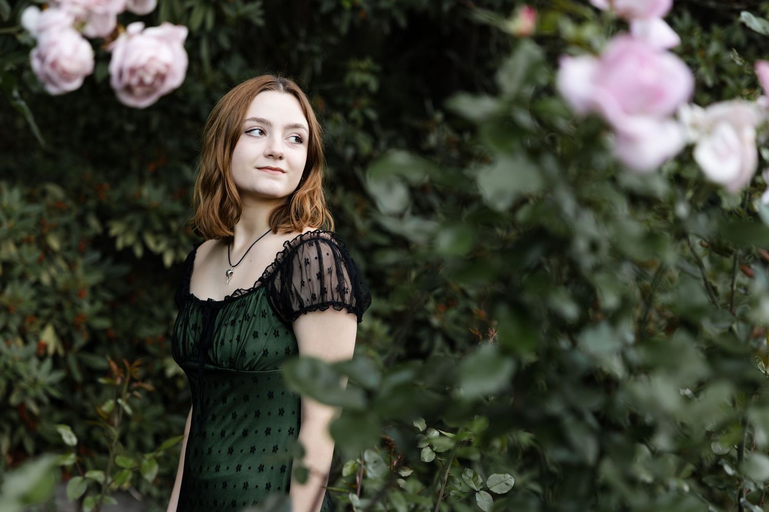 A romantic portrait with pink roses in a garden setting, featuring a dark lace dress and natural lighting.