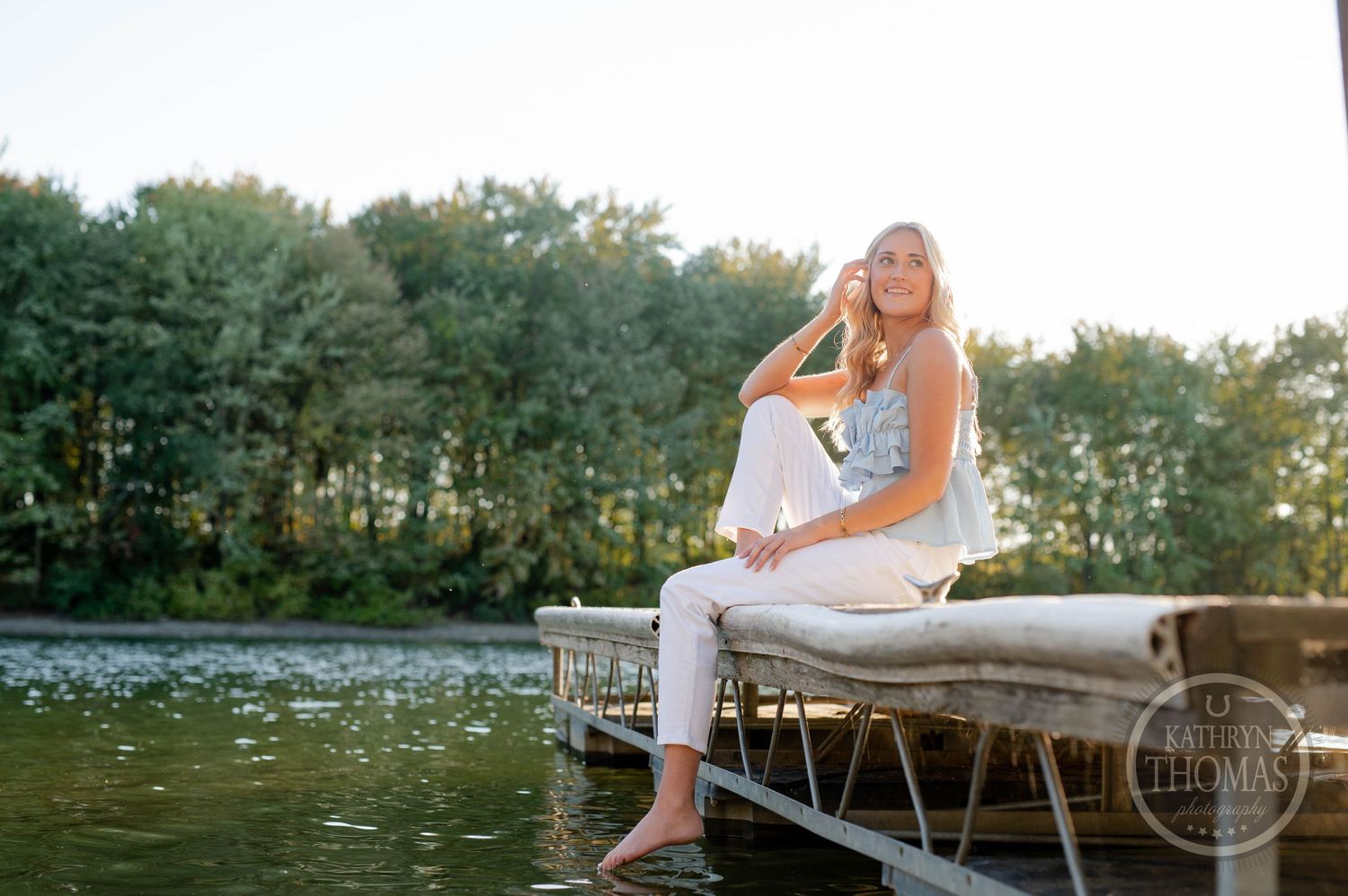 Casual outdoor photo session on lake dock with person in blue top and white pants.