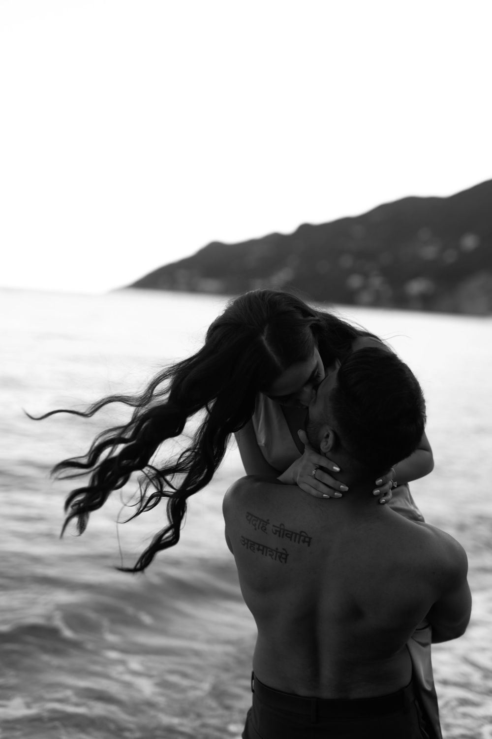 A black and white series of photos showing an intimate embrace at the beach, with windswept hair flowing in the breeze.