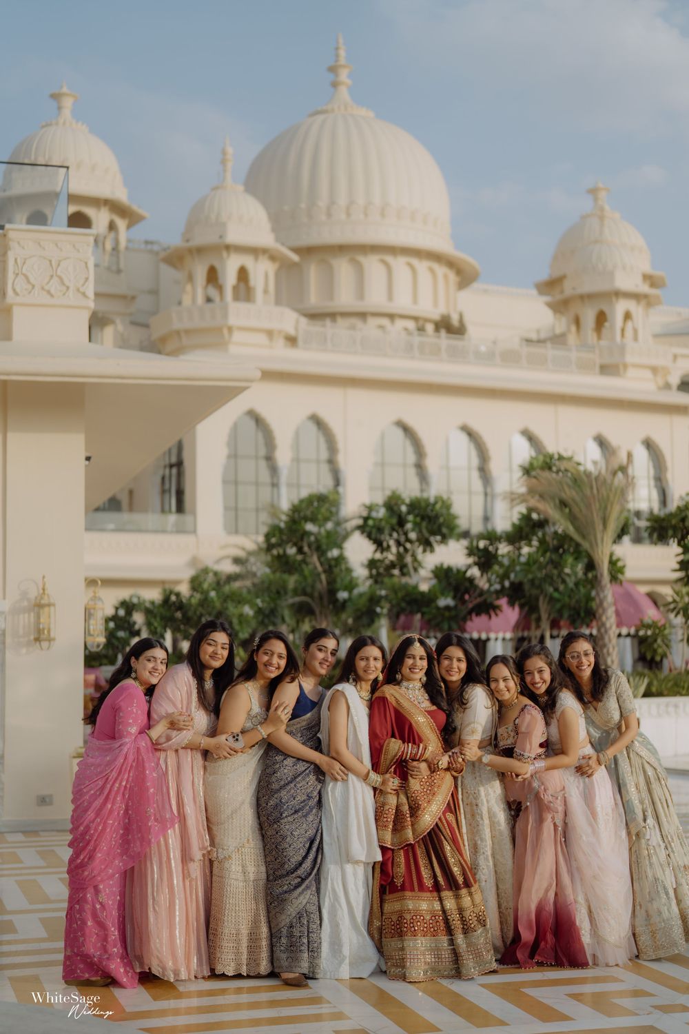 A group in colorful traditional Indian attire poses in front of a grand white domed palace with ornate architecture.