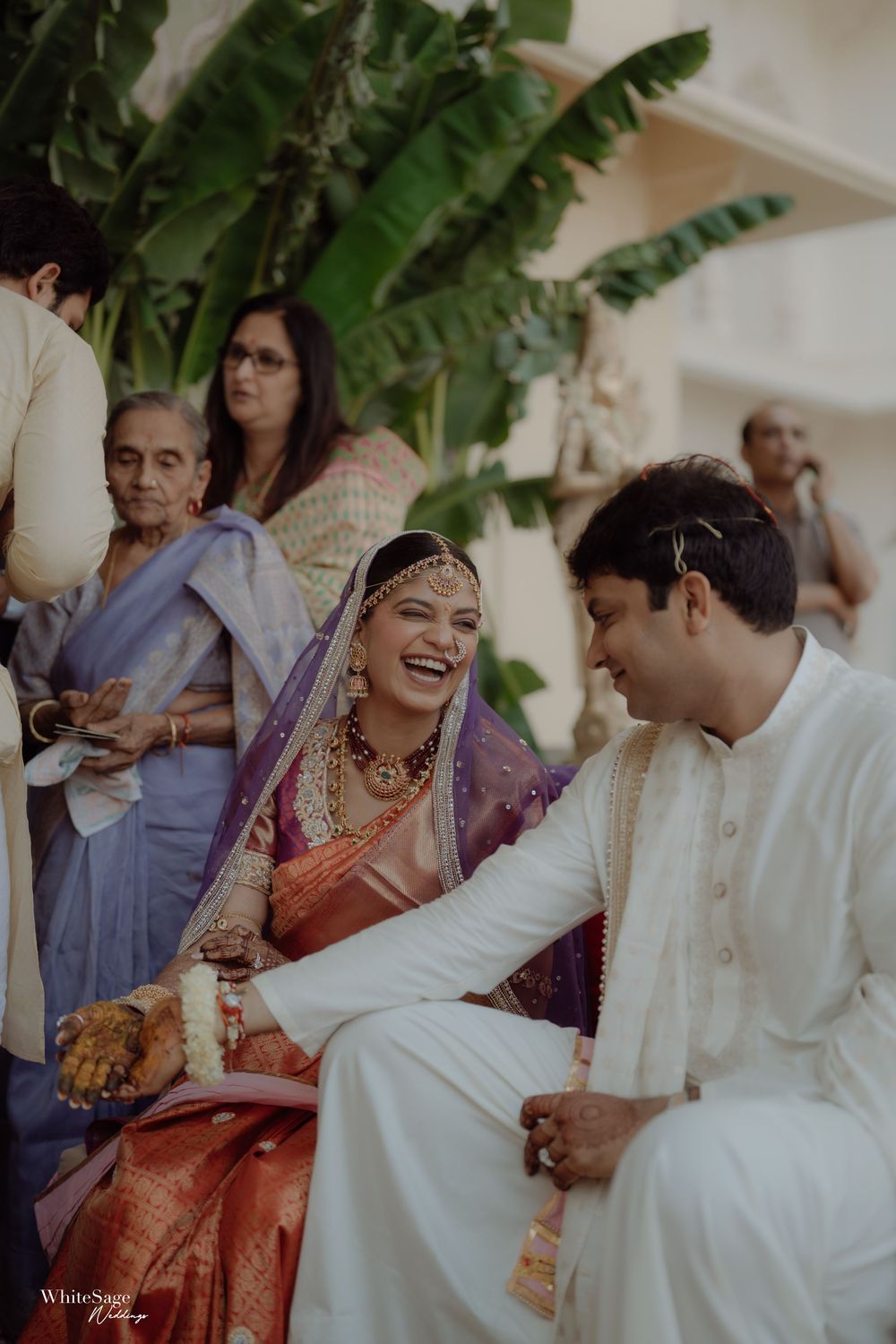 A couple celebrates during their traditional Indian wedding ceremony as guests gather in an outdoor setting.