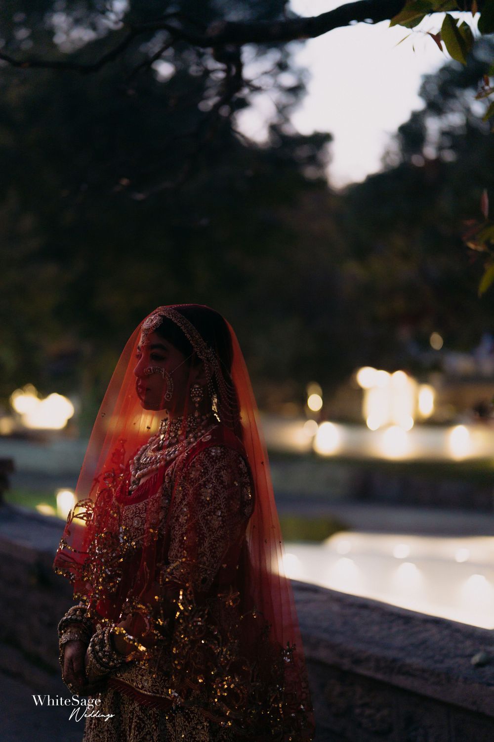 Silhouette of a bride in a red traditional Indian outfit against evening bokeh lights.