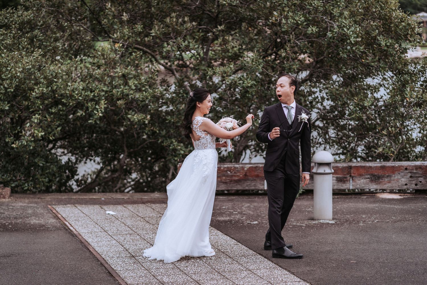 A wedding couple dances joyfully together on a paved outdoor terrace surrounded by greenery.