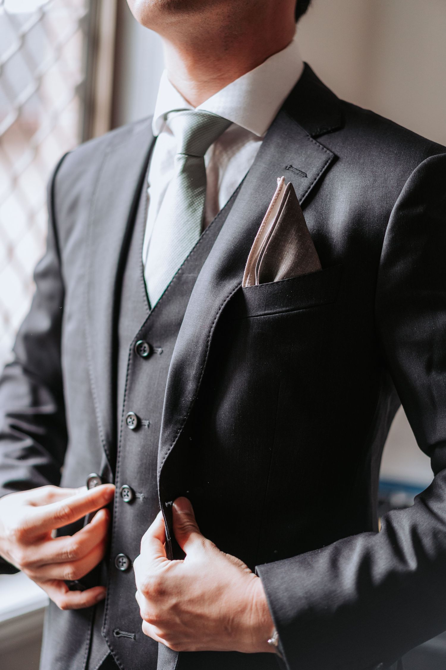 Close-up of a stylish charcoal grey three-piece suit with pocket square and mint green tie.