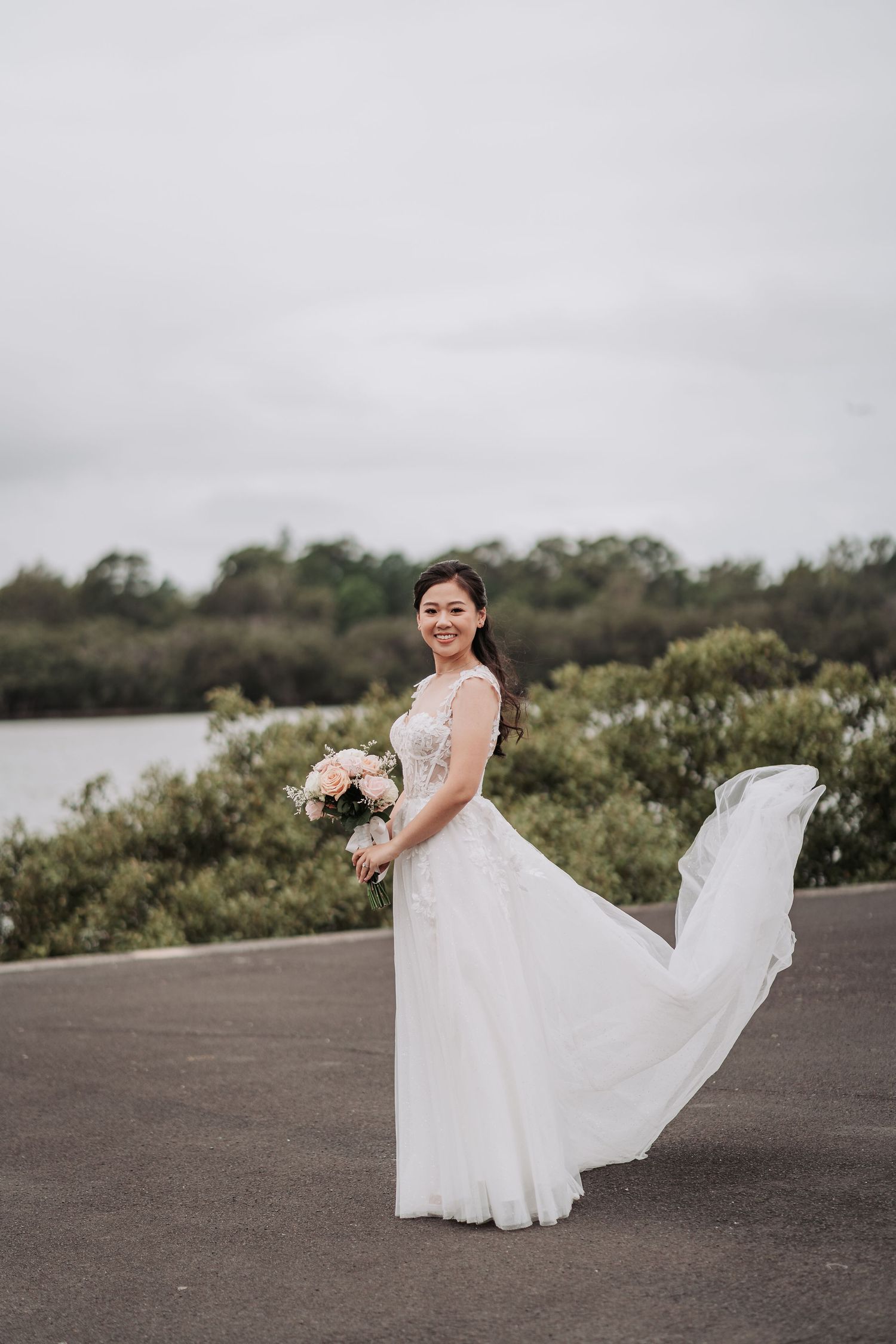 An elegant white wedding gown with flowing train captured against a scenic waterfront backdrop.