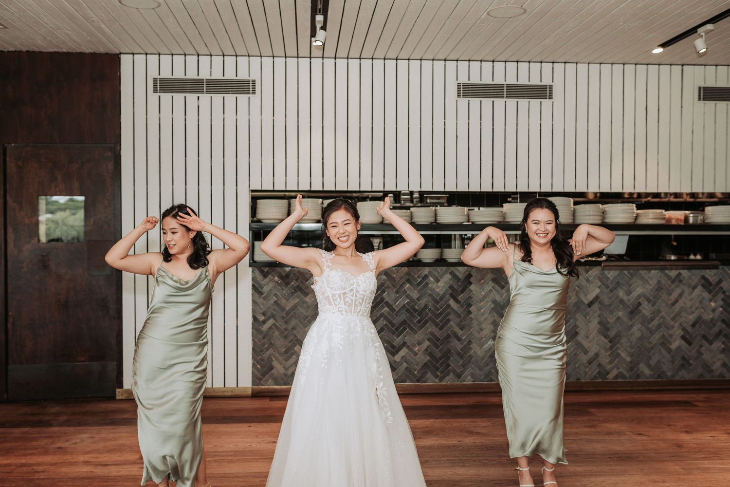 Wedding party strikes fun poses with the bride in white and bridesmaids in sage green dresses.