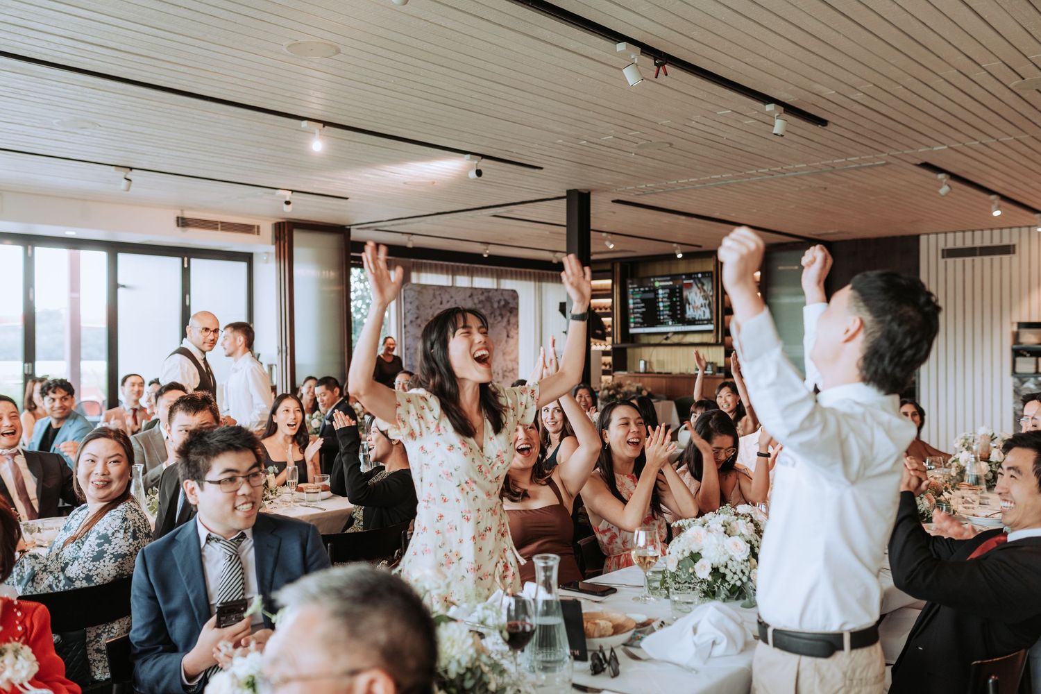 Wedding reception guests celebrating and raising their hands in joy at a modern venue.
