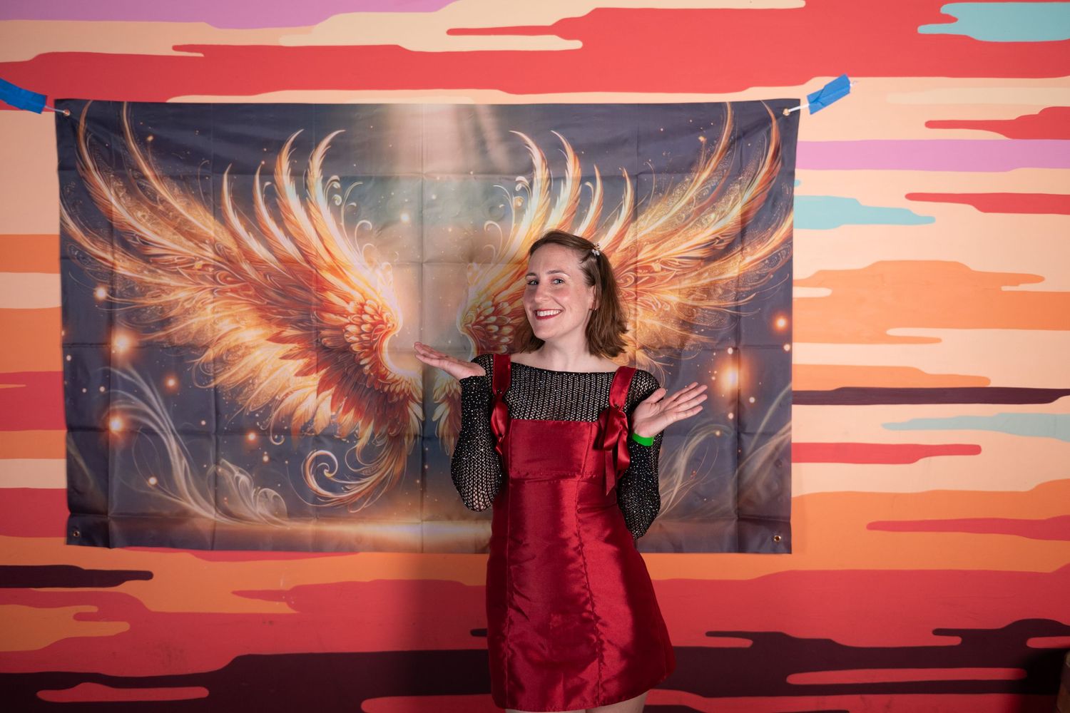 People pose in front of a vibrant sunset backdrop with glowing wings artwork at a photo booth.