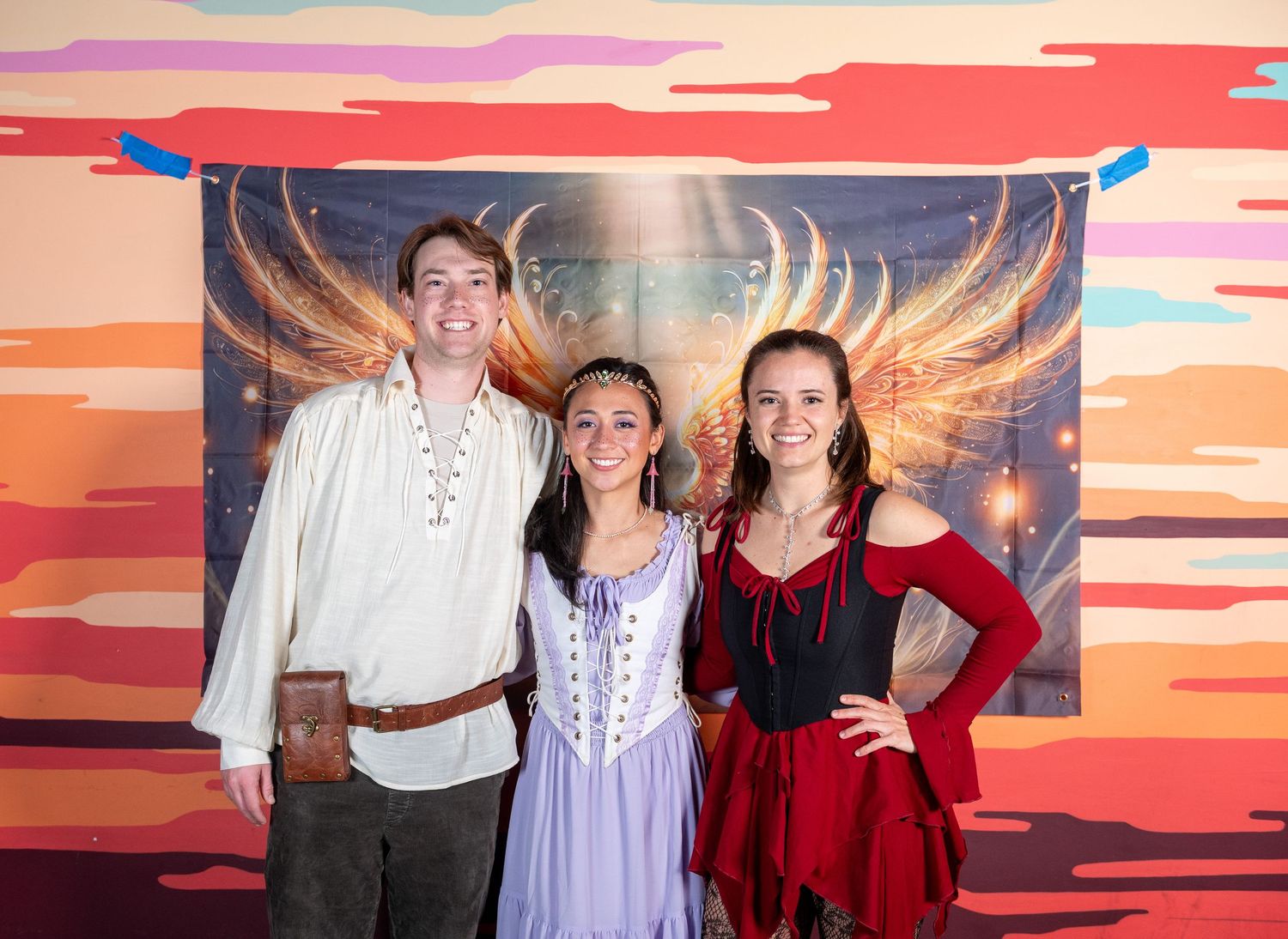 Group in formal wear gathered by decorative wing mural with warm lighting effects.