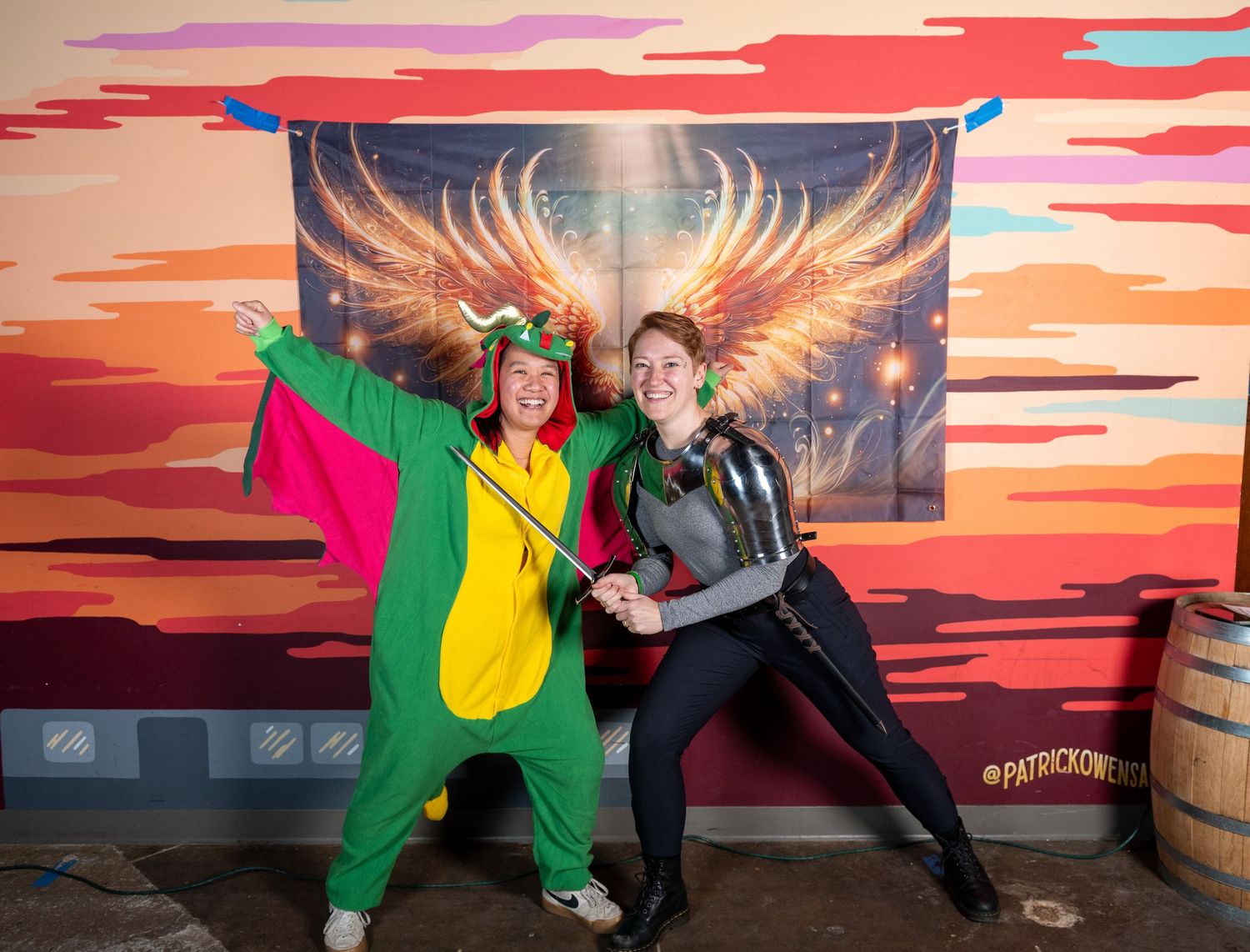 People pose playfully in front of a colorful wall mural featuring golden wings and sunset colors.