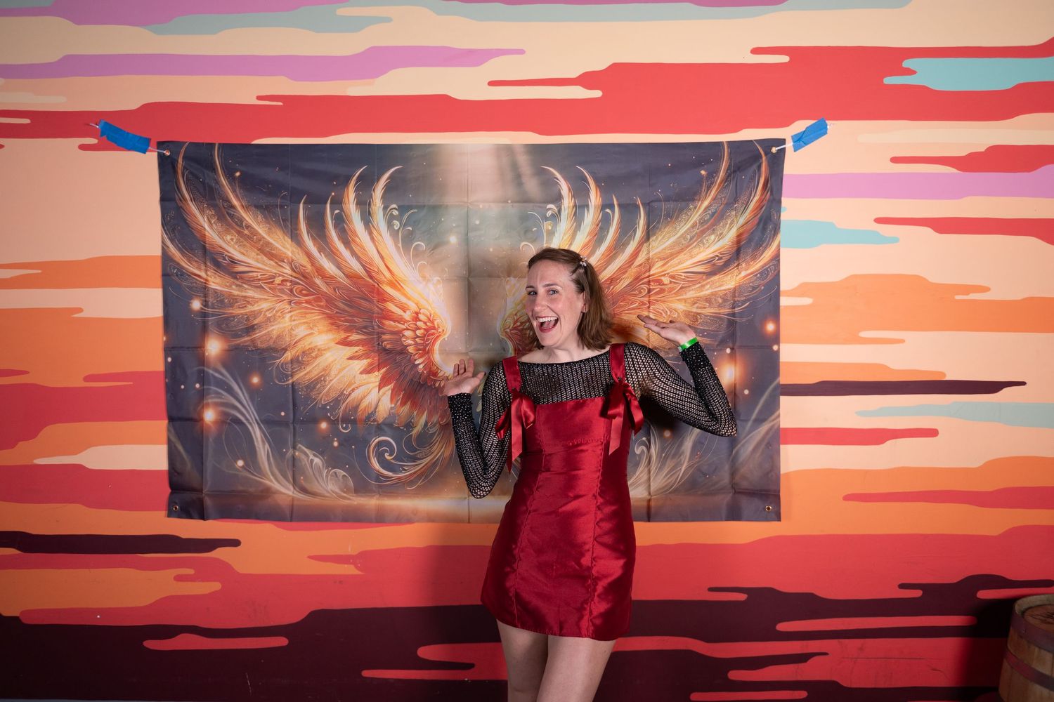 People posing in front of a vibrant sunset mural with golden wings and red-orange clouds.