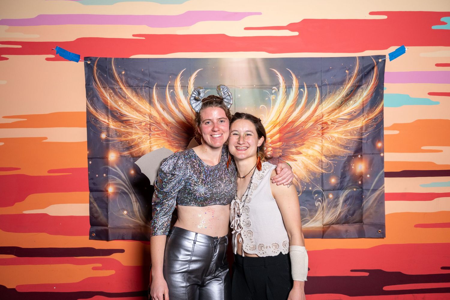 Friends gather for photo against dramatic orange sunset wall with illuminated angel wing artwork.