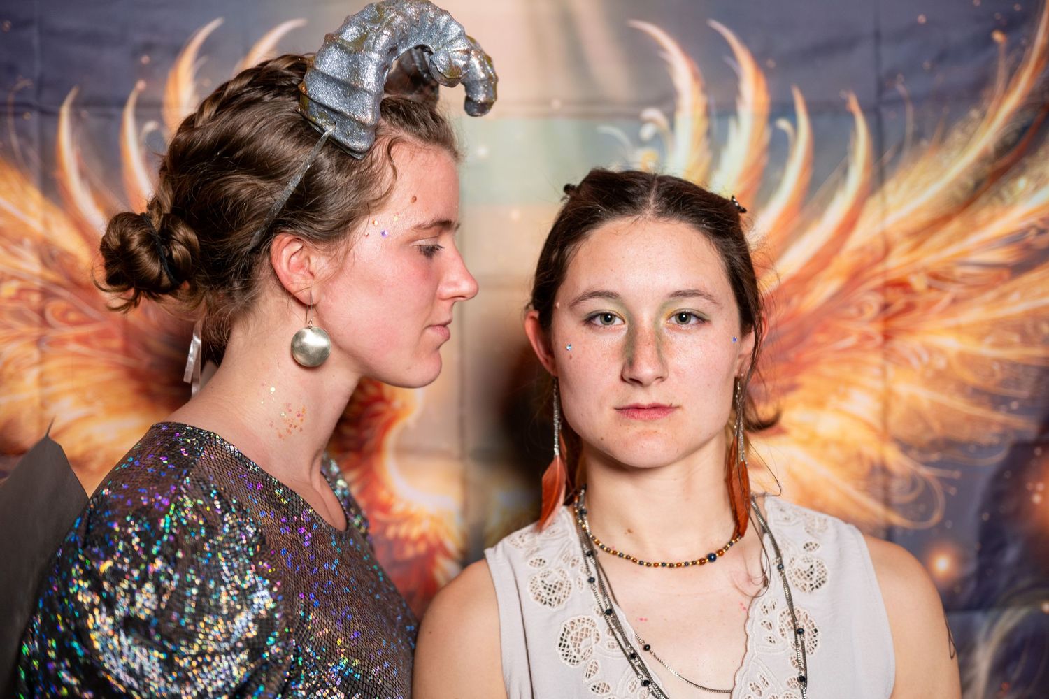 Friends smile and embrace near illuminated angel wing art installation.