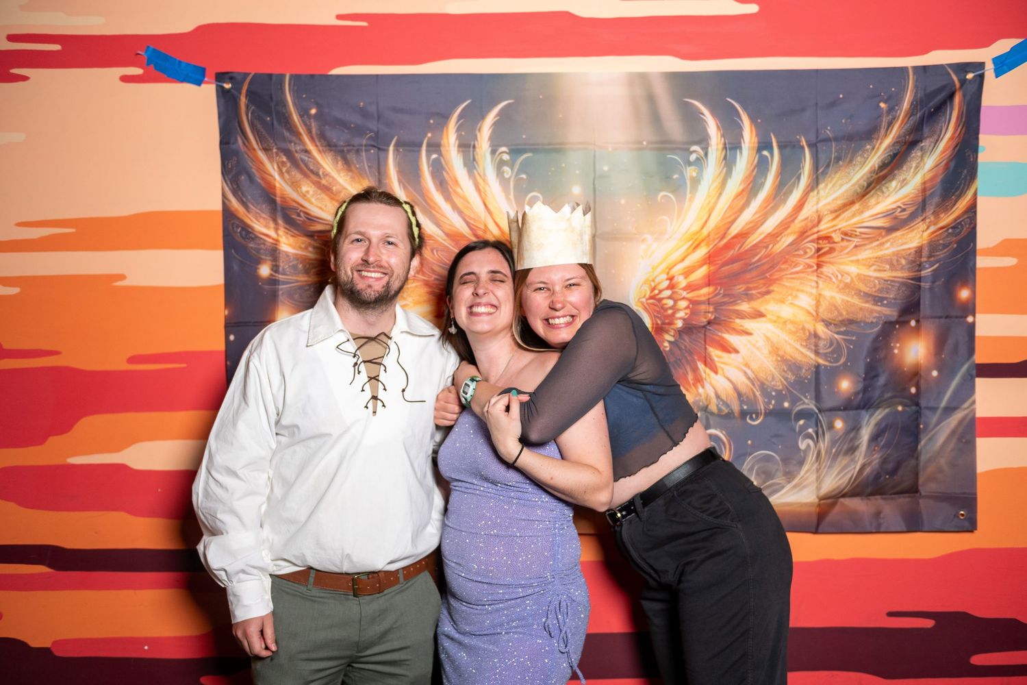 Party guests pose together at photo station featuring fiery sunset colors and glowing wing display.