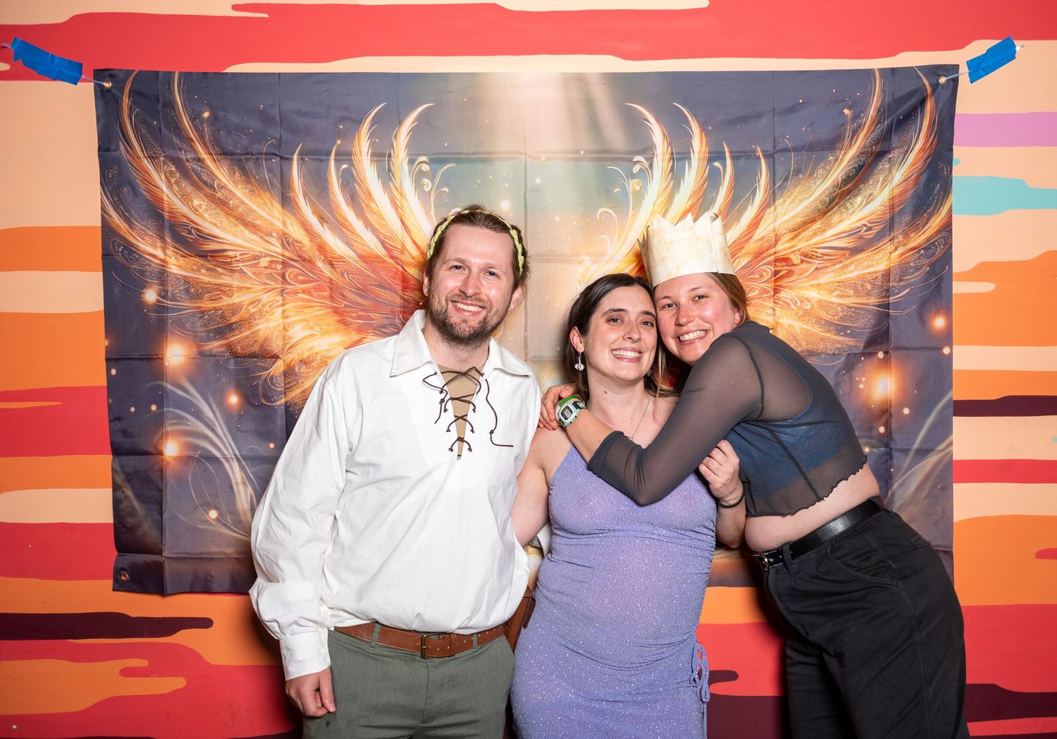 A sequence of photo booth shots featuring people having fun against an orange and red sunset mural with illuminated wings.