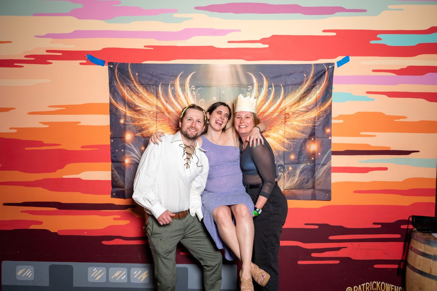 Group strikes playful poses in front of illuminated wing mural with sunset background.