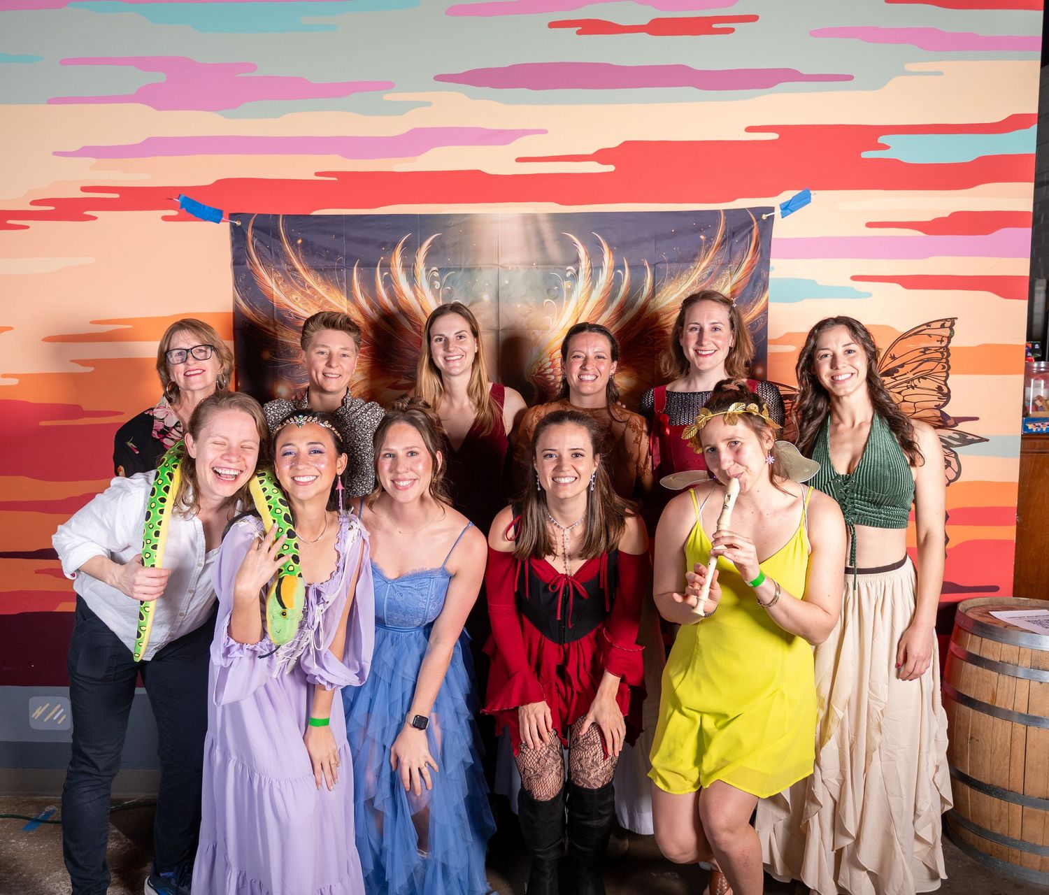 Group of friends in colorful outfits pose together against sunset-themed wall art.