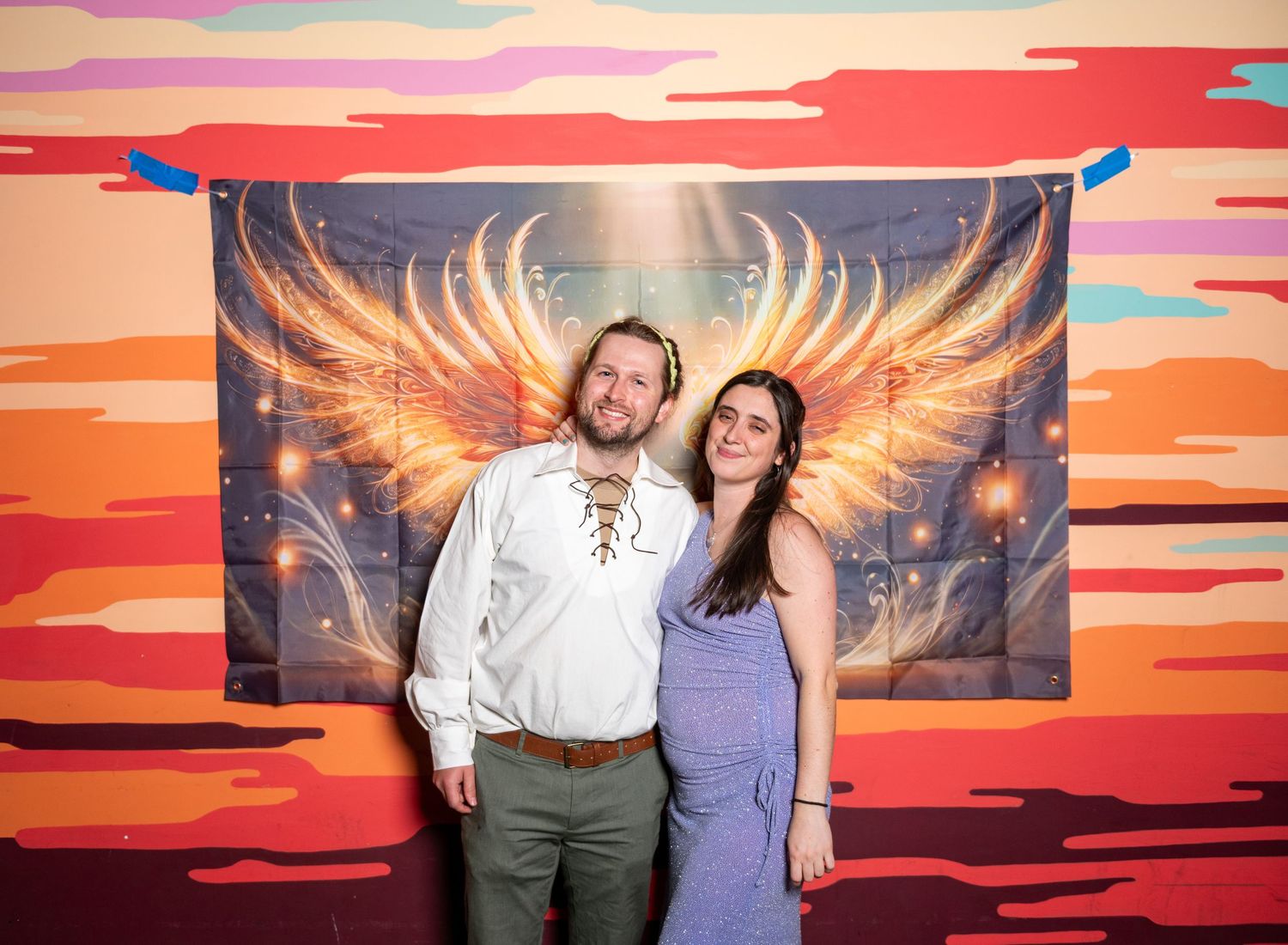 People enjoying photo opportunity with dramatic sunset mural and golden wing art installation.