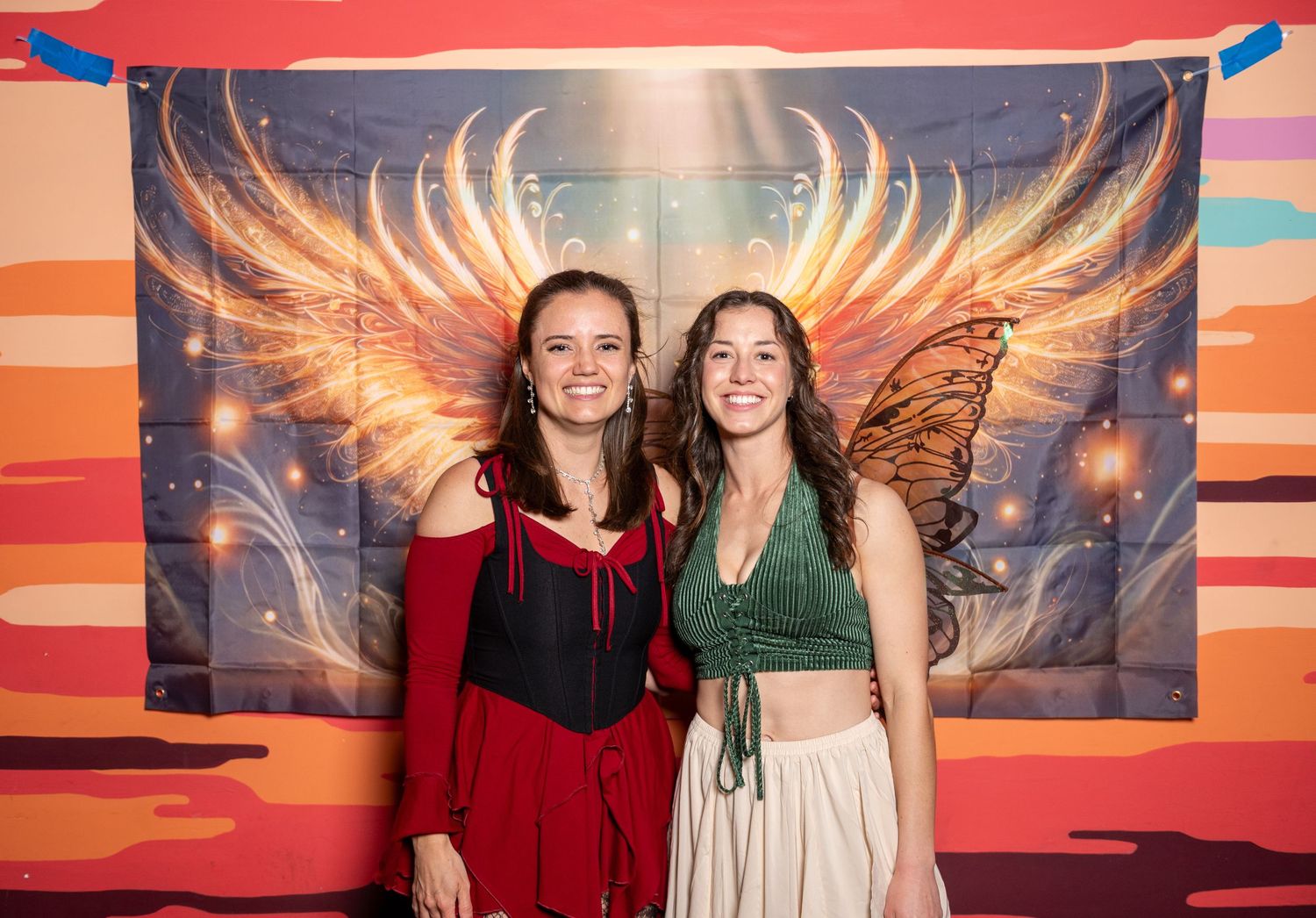 Friends posing together against a dramatic wall mural with golden wings and sunset hues.