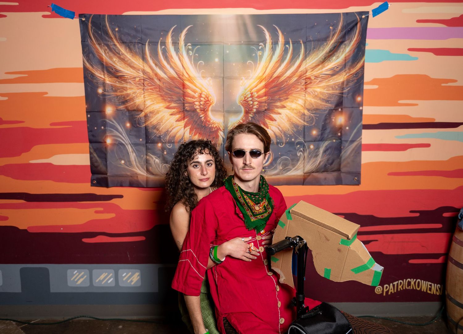 Party guests strike poses in front of a sunset-themed backdrop with glowing wing design.