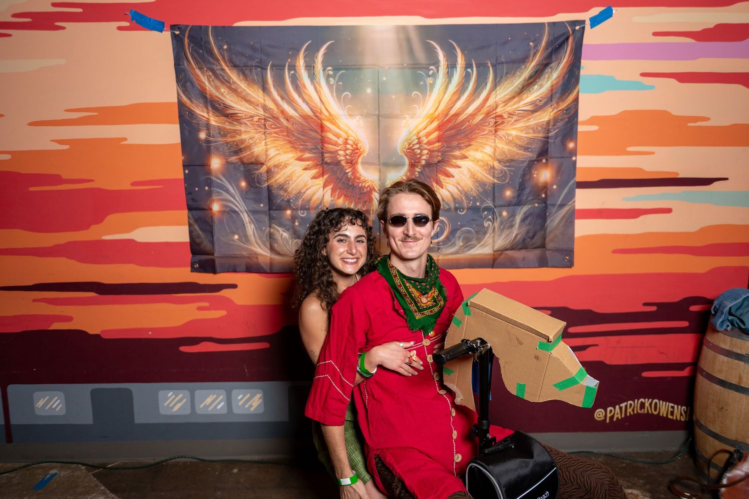Group enjoys photo opportunities in front of artistic sunset wall with illuminated wing design.