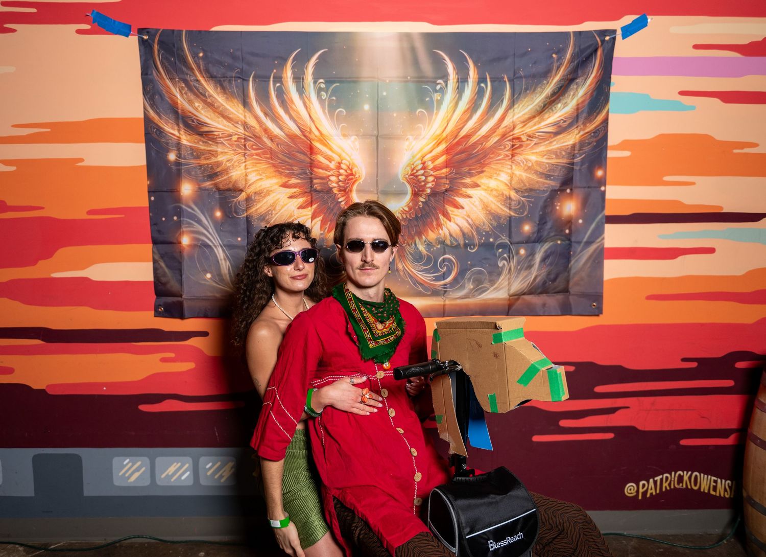 Friends having fun at a photo booth with sunset background and golden wing artwork.