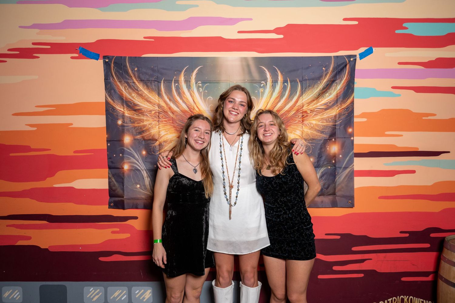 Group photo session in front of a vibrant angel wing mural with sunset colors.
