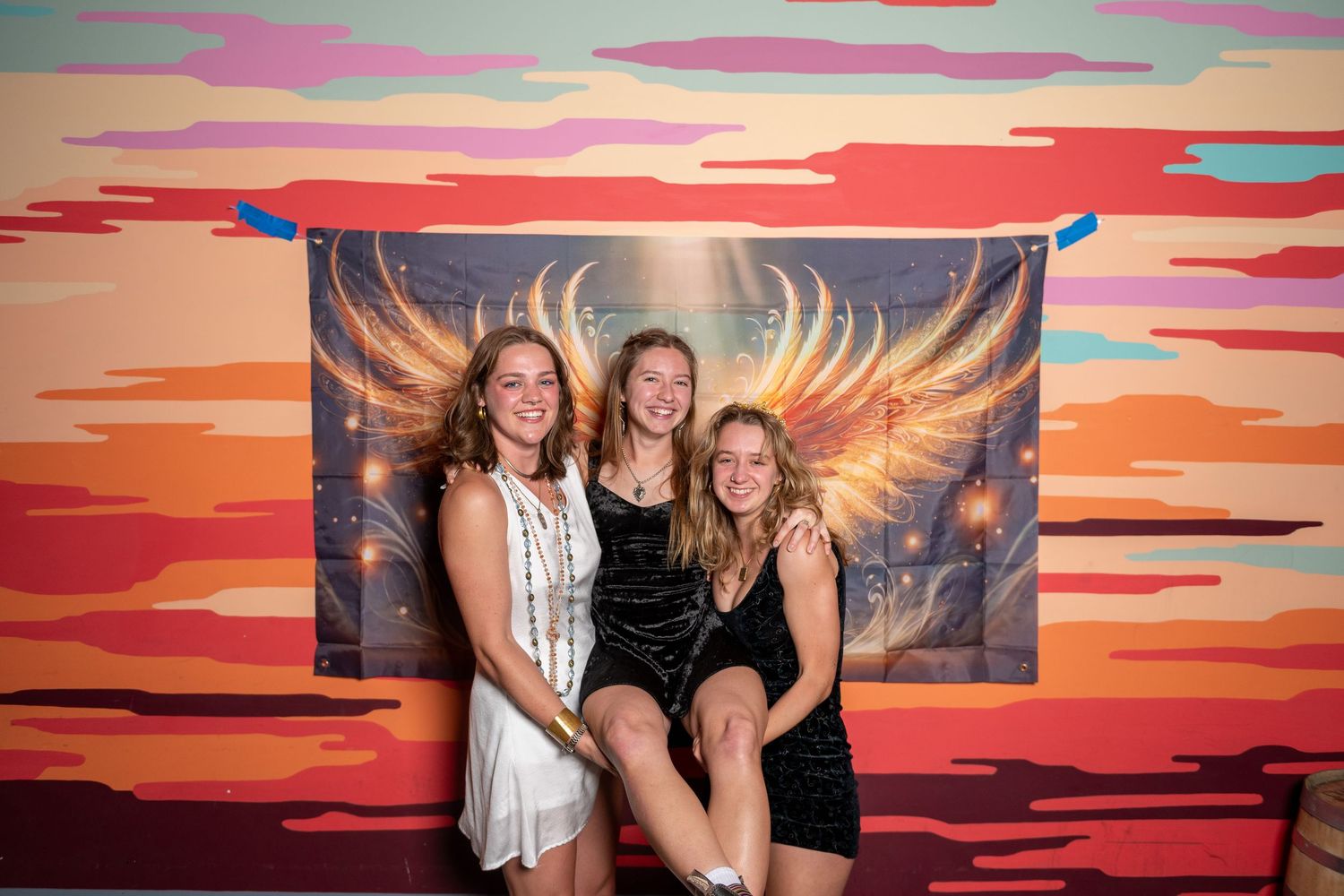 People pose energetically in front of sunset-themed backdrop with golden wing design.