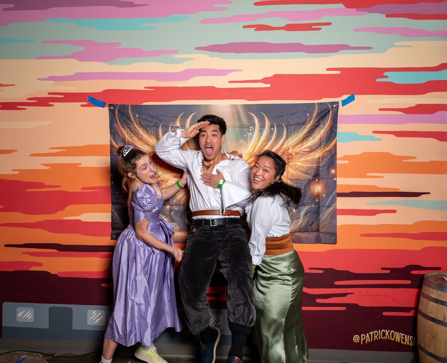 A group of performers dance and pose in front of a vibrant sunset-colored backdrop on stage during a theatrical show.