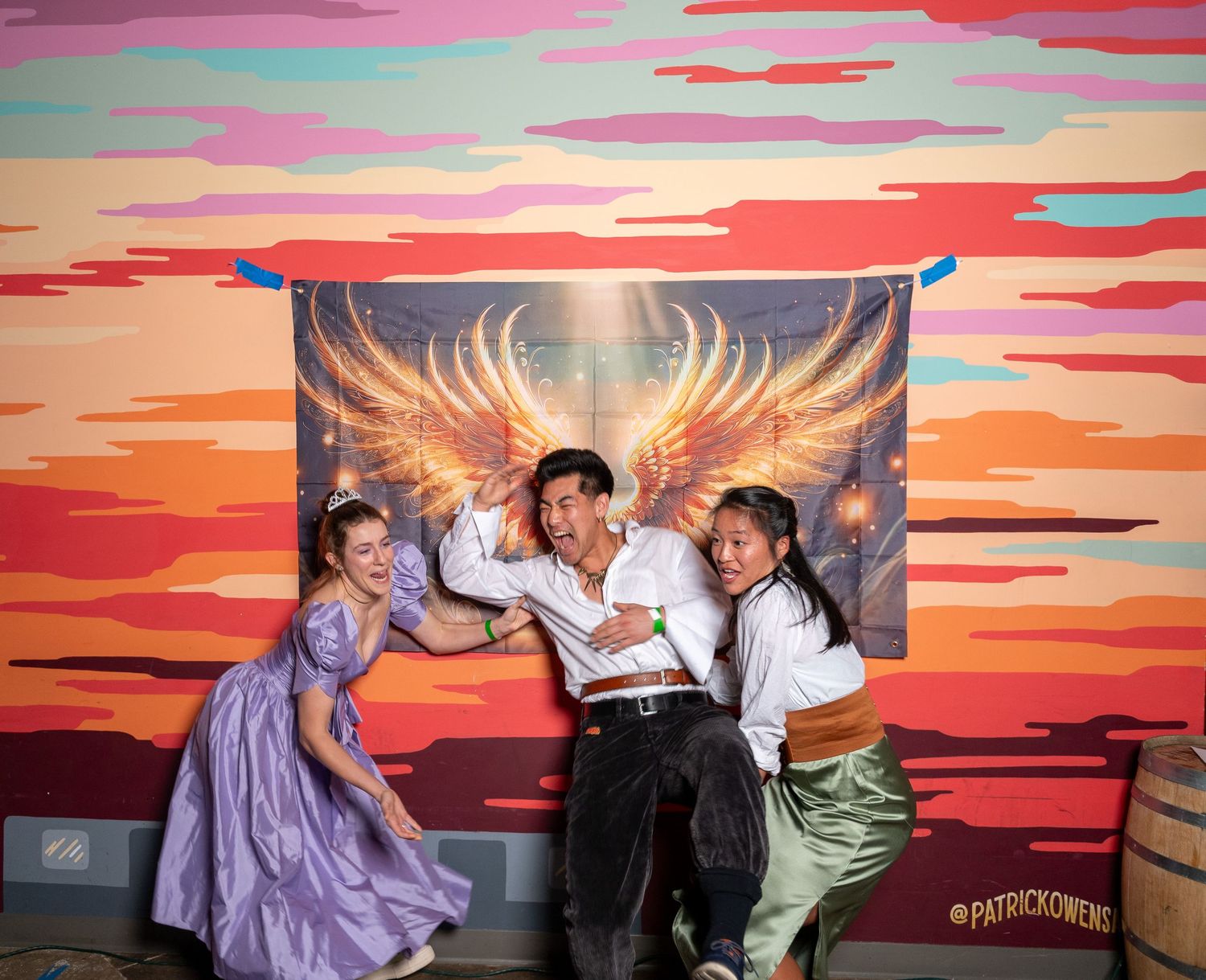 People having fun posing against a dramatic sunset mural with golden wing artwork.