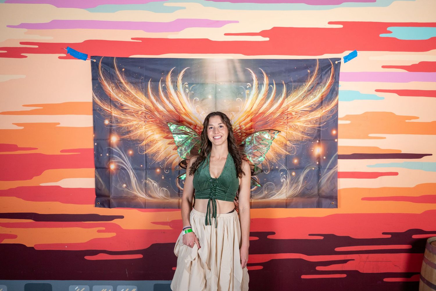 Friends gather for photos against colorful wall art featuring fiery wings and sunset hues.