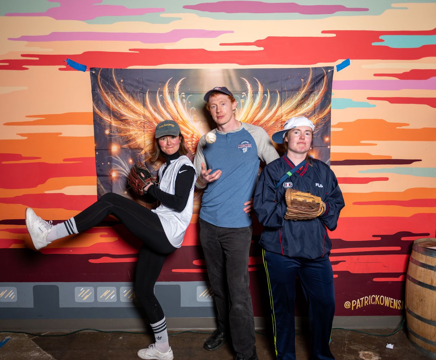 A group of people pose together against a vibrant sunset-colored wall mural in an urban setting.